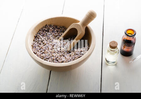 Bol en bois plein de boutons de fleurs de lavande séchées avec, à côté des flacons en verre remplis de l'huile sur planche en bois laqué blanc table.. Banque D'Images