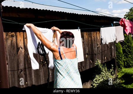 Vue arrière d'une femme en robe de chambre typique tout en raccrochant les vêtements à l'extérieur de la maison pour bien sécher. String et collier vêtements bof Banque D'Images