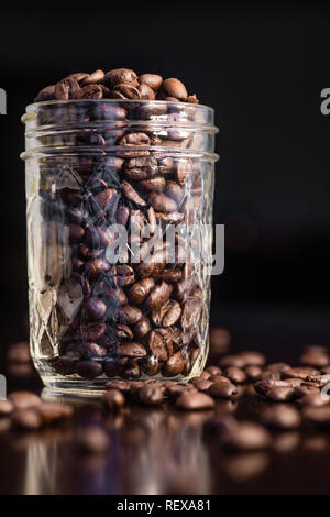 Grains de café dans un bol en verre et déversés sur la table Banque D'Images