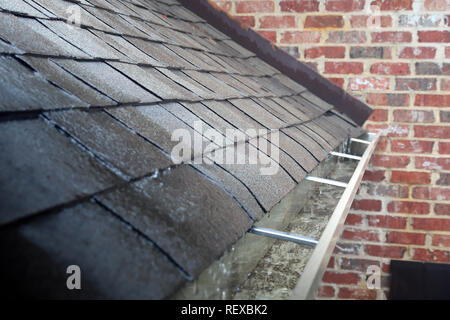 Gouttière de travail sur une maison en brique avec l'eau qui coule dans l'herbe pendant la tempête de pluie Banque D'Images