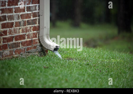 Gouttière de travail sur une maison en brique avec l'eau qui coule dans l'herbe pendant la tempête de pluie Banque D'Images