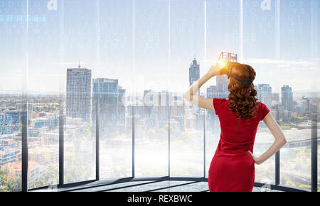 Femme en robe rouge portant un casque de réalité virtuelle. Technique mixte Banque D'Images