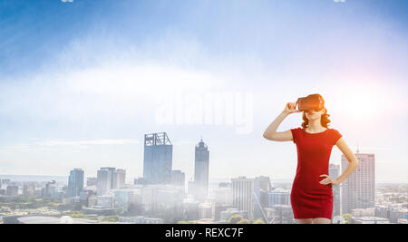 Femme en robe rouge portant un casque de réalité virtuelle. Technique mixte Banque D'Images