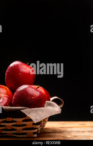 Tas de pommes rouges humides situées dans bol tressé sur fond noir Banque D'Images