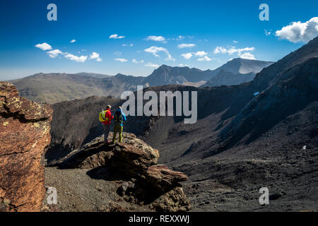 Vue arrière de deux voyageurs masculins debout sur rock et en regardant les montagnes magnifiques sur belle journée ensoleillée en Sierra Nevada, Granada, Espagne Banque D'Images