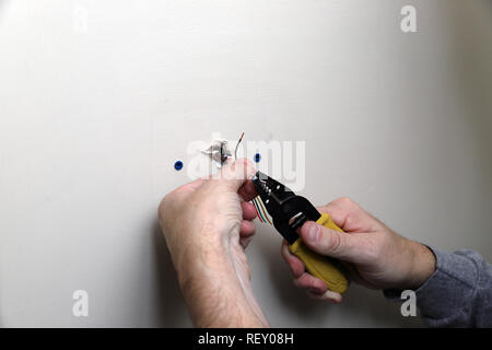 Close-up of hand holding pour le fil de commande de thermostat avec une unité de chauffage, ventilation et climatisation, venant de mur au cours de l'installation Banque D'Images