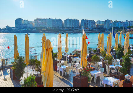 ST Julians, Malte - 20 juin 2018 : l'agréable terrasse du restaurant sur la côte d'exilés Bay avec une vue sur les bateaux et l'édifice moderne Banque D'Images