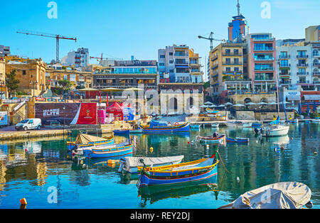 ST Julians, Malte - 20 juin 2018 : les bateaux de pêche dans la baie de Spinola Harbour avec des immeubles d'habitation modernes et cafés côtières sur l'arrière-plan, sur J Banque D'Images