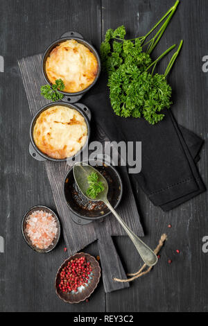 Shepherd's pie, de la cocotte en fonte casserole, avec la viande hachée, la purée de pommes de terre et légumes, sur fond sombre, la composition verticale Banque D'Images
