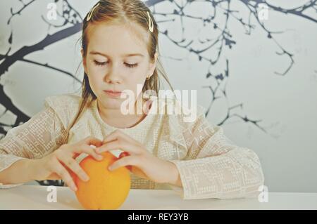 White Caucasian girl (enfant, kid) essayer de déballer une orange à la main Banque D'Images
