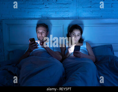 Jeune couple au lit tard dans la nuit avec les téléphones intelligents obsédé avec des jeux, des médias sociaux et de l'ignorant dans les applications pb communication relation Banque D'Images