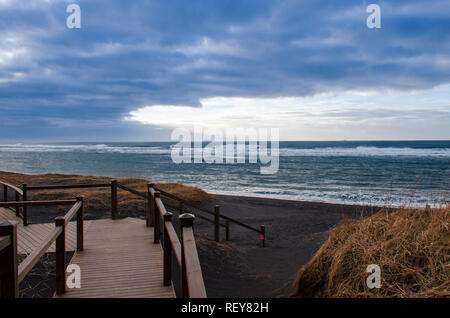 Un escalier en bois mène à une plage de sable volcanique noir sur les rives de l'océan Atlantique en Islande Banque D'Images