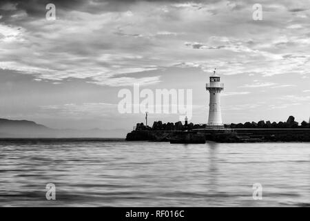 Impression de gris de blanc phare solitaire sur le bout de mur brise-lames de grès protéger le port de la ville de Wollongong vagues du Pacifique. Banque D'Images