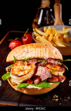 Terre et Mer gastronomique fruits de mer et viandes burger avec rosé rôti de boeuf, crevettes, pois mange-tout, tomates et roquette servis avec frites Banque D'Images