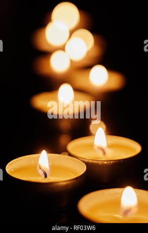 Bougies votives brûlant dans l'obscurité dans une église ou au cours d'une veillée du souvenir dans la nuit avec un arrière-plan flou DOF et peu profondes Banque D'Images