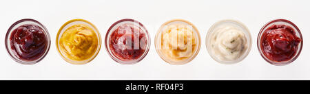 Ligne d'un assortiment de trempettes, sauces et marinades vue d'en haut isolé sur blanc dans de petits bols en verre dans un panorama banner Banque D'Images