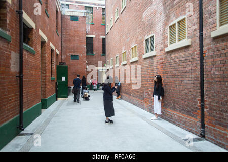 Groupe de visiteurs prenant des photos ou posant contre le mur de briques au centre Tai Kwun, à Hong Kong. Banque D'Images