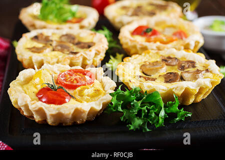 Les champignons, cheddar, tomates tartelettes sur fond de bois. Mini tartes. Délicieux apéritif, tapas, snack. Banque D'Images