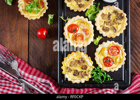 Les champignons, cheddar, tomates tartelettes sur fond de bois. Mini tartes. Délicieux apéritif, tapas, snack. Vue d'en haut. Mise à plat Banque D'Images