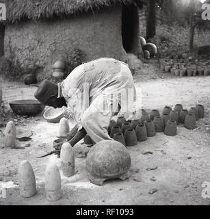 Années 1950, historiques, de vêtements traditionnels africains locaux Yoruba hat, un Aso Oke hat et le chiffon robe, faire des pots d'argile à l'extérieur de sa hutte, le Nigeria, l'Afrique. Banque D'Images