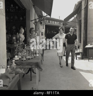 Années 1950, historique, Paris, un jeune couple se promener passer la cale à un second-hand, vintage un marché en plein air de la ville. Paris a beaucoup de ces marchés extérieurs et intérieurs", souvent appelée "marchés aux puces", venant de l'anglais 'Marche aux puces', nom donné à l'origine d'un marché à Paris qui a vendu des biens meubles shabby utilisé et de la nature qui peuvent contenir des puces ! Banque D'Images