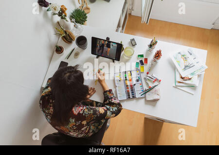 Illustrator en peinture à un bureau dans un atelier à l'aide de tablette numérique, vue du dessus Banque D'Images