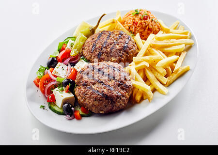 Les boulettes de viande épicées bifteki grec servi avec une salade fraîche, chips de pomme de terre et tomate riz pilaf ou domatorizo sur un plateau ovale sur fond blanc Banque D'Images