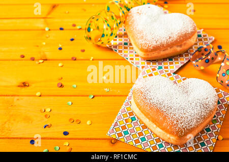 Couple de beignets en forme de coeur romantique sur serviettes en papier de couleur jaune sur une table en bois avec des confettis et copy space Banque D'Images