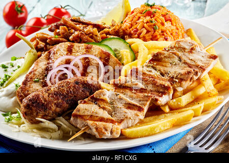 Plaque grill grec avec un assortiment de viandes, croustillant de croustilles de pommes de terre, tomate riz pilaf et raiti dans une vue en gros convient pour un menu Banque D'Images