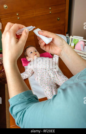 Mains de mère versant sérum pour nettoyer les yeux de bébé Banque D'Images