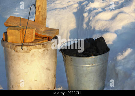 Deux seaux remplis avec du charbon et du bois sont debout sur la neige. La préparation pour la saison de chauffage dans le village. Banque D'Images