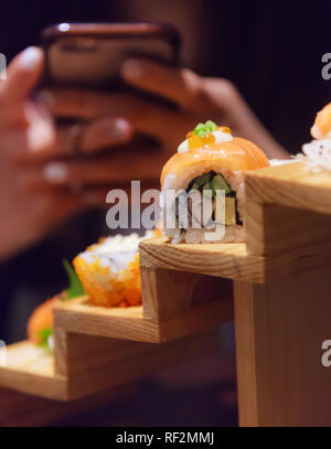 Utilisation femme prendre smartphone photo sur du poisson frais, des aliments japonais rouleaux de sushi Saumon Assortiment décoration sur des marches de bois traditionnelle japonaise en restaura Banque D'Images