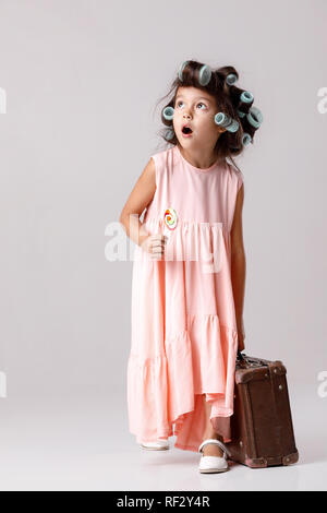 Funny little girl en robe rose et les bigoudis holding lollipop Banque D'Images