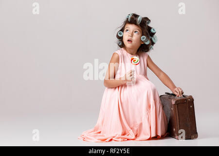 Funny little girl en robe rose et les bigoudis holding lollipop Banque D'Images