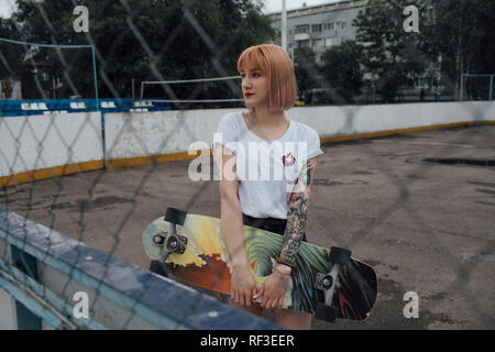 Cool young woman holding carver skateboard en plein air Banque D'Images