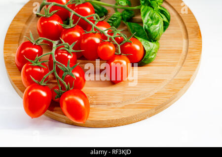 La branche de tomates cerise sur un fond de bois. Les tomates cerise et les feuilles de basilic sur un fond blanc. Banque D'Images