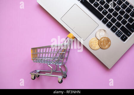 Photo conceptuelle de l'e-commerce en utilisant cryptocurrency. Ordinateur, panier et pièces Bitcoin ou cryptocurrency sur un fond rose. Banque D'Images