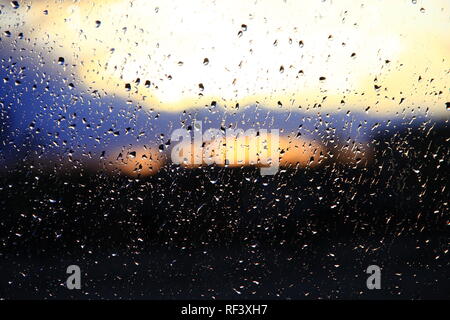 La pluie à l'extérieur fenêtre sur fond de coucher du soleil. Gouttes de pluie sur le verre au cours de la pluie. Coucher du soleil à l'extérieur fenêtre pendant les jours de pluie. La texture lumineuse de gouttes d'eau Banque D'Images