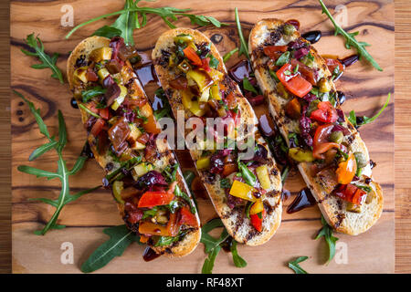 Bruschetta de tomates savoureuses avec les câpres, la roquette, un assaisonnement balsamique servi sur une planche à découper en bois Banque D'Images