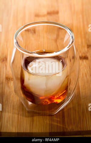 Straight whiskey servi dans un whisky double paroi en verre, servi avec une sphère de glace servi sur une barre en bois haut Banque D'Images