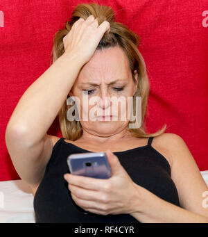 Desperate woman looking at her smartphone allongé sur le lit dans un tank top Banque D'Images