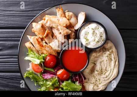 Plaque avec du poulet shawarma sain, hoummos, salade et sauces close-up sur une table en bois. haut horizontale Vue de dessus Banque D'Images