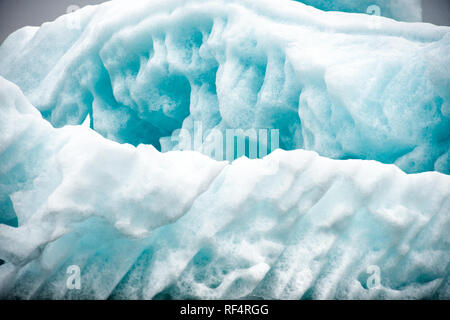 Hornsund | HORNSUND, Svalbard — Les crevasses ensoleillées à la surface d’un iceberg tracent les lignes de flux stratifiées de la glace glaciaire compressée sur des années avant de se détacher dans le fjord. Les glaciers de mer de Hornsund, parmi les plus rapidement en recul à Svalbard, libèrent continuellement des fragments comme celui-ci dans l’eau sous le Hornsundtind et les sommets environnants. Banque D'Images