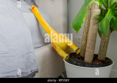 Dinosaure jouet jaune tombé sur le côté du lit, dans un cache-pot, représentant une maison familiale et de la vie de parent. Banque D'Images