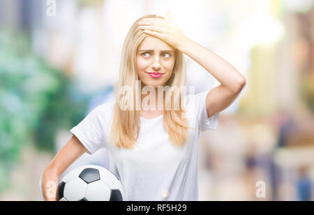 Belle jeune femme blonde holding soccer ball sur fond isolé a souligné avec la main sur la tête, choqué par la honte et l'effet de surprise, en colère et face Banque D'Images