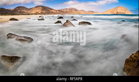 L'eau se déplaçant entre les rochers à une plage sauvage dans le désert d'Atacama. Le mouvement de l'eau crée des formes dans l'eau sur une longue exposition Banque D'Images