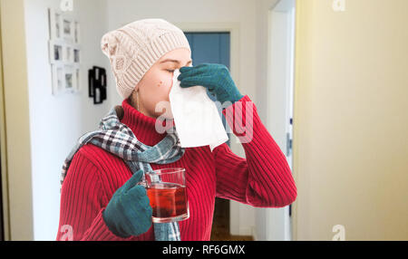 Woman holding transparent tasse de thé portant des vêtements et accessoires de l'hiver soufflant le nez avec une serviette blanche comme concept saison froide Banque D'Images