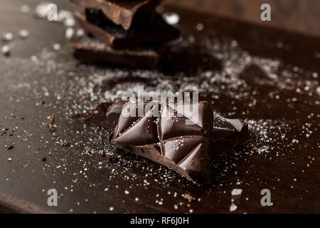 Morceaux de chocolat amer à la fleur de sel sur la surface en bois sombre. Des collations bio.
