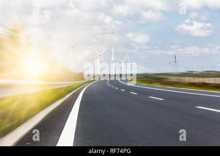 Les éoliennes sur le paysage le long de la route vide contre ciel. Banque D'Images