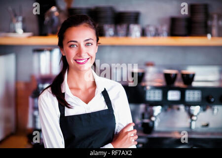 Portrait of smiling waitress standing with arms crossed Banque D'Images